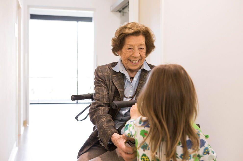 Eine alte Dame die auf Ihrem Rollator sitzt und ein Kind vor Ihre anlächelt